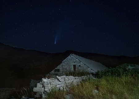 Long period comet C/2020 F3 (NEOWISE) with tail visible in night sky above the Dinara mountain in Dinaric Alps on the border between Croatia and Bosnia and Herzegovina. Illuminated hut on foreground.の写真素材