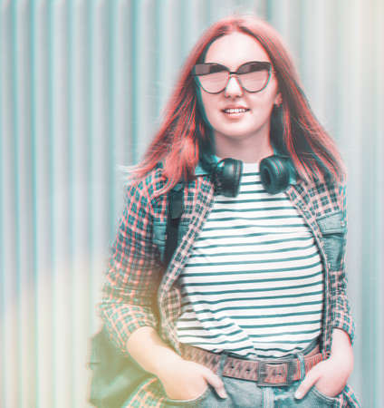 Glitched portrait of a beautiful modern smiling young female teenager with extraordinary hairstyle color in a checkered shirt and mirrored sunglasses portrait with headphones hanged on neck.の写真素材