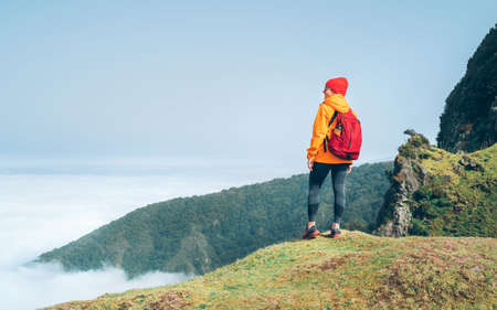 Young female backpacker dressed orange waterproof jacket hiking by the mountain above the cloud route at the end of February on Madeira island,Portugal. Active people around a World traveling conceptの写真素材