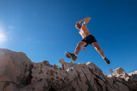 Active fast running mountain sweaty body muscular sky runner jumping over the cleft cliff during the morning jogging. Sporty people activities wide-angle concept image.の写真素材