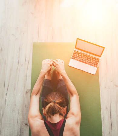 Fit sporty healthy woman sitting on mat in Paschimottanasana pose, doing breathing exercises, watching online yoga class on laptop computer. Healthy people and self motivation Top view concept.の写真素材