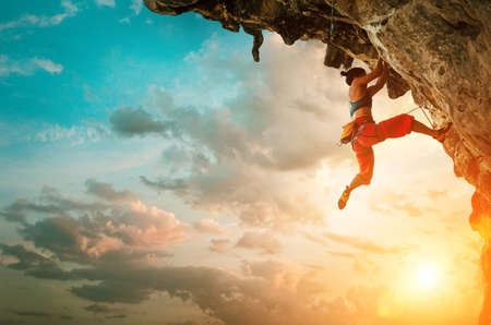 Athletic Woman climbing on overhanging cliff rock with sunset sky backgroundの写真素材