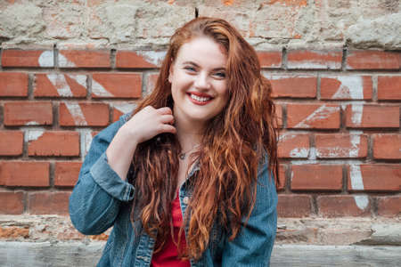 Sincerely smiling Red curled hair caucasian teen girl with blue eyes fashion portrait on the red...