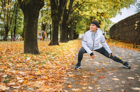 Fit athletic woman doing workout before jogging in the autumnal city park on the kids playground. Young fitness female runner stretching legs while warming up. Active runners people concept image.の写真素材