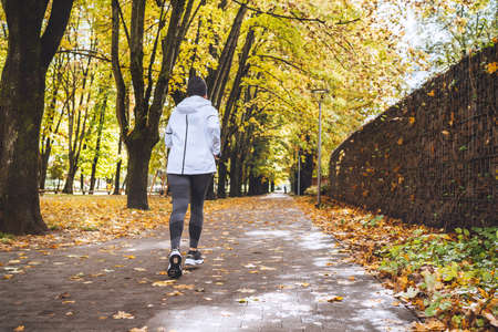 Fit athletic woman have a jogging in the autumnal city park. Young fitness female running by the...