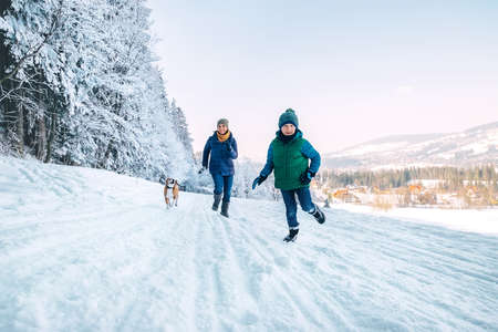 Mother and son having a fun during dog walk. They running with their beagle dog in snowy forest. Mother and son relatives and femily values concept image.の写真素材
