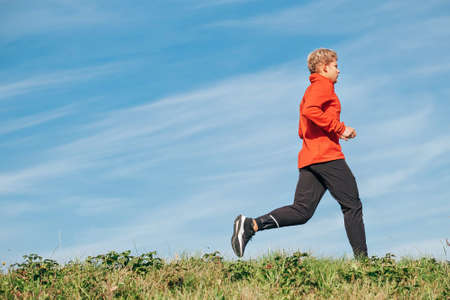 Man dressed in red long sleeve shirt, black running trousers and shoes running by the road with blue sky background. Sporty people activities and a healthy lifestyle concept image.の写真素材