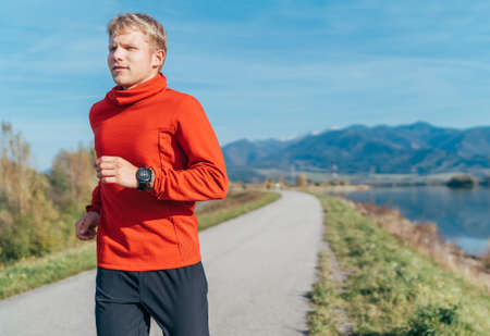 A man dressed in red long sleeve shirt have a morning jogging by the road with a mountain background. Sporty people activities and a healthy lifestyle concept image.の写真素材