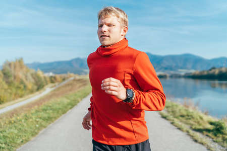 A man dressed in red long sleeve shirt have a morning jogging by the road with a mountain background. Sporty people activities and a healthy lifestyle concept image.の写真素材