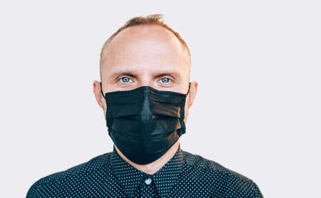 Portrait of man using a black facial mask during a COVID-19 world pandemic looking at camera....
