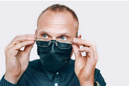 Portrait of man taking off glasses in black facial mask during a COVID-19 world pandemic looking at camera. Virus self-protection and vision health concept image.の写真素材