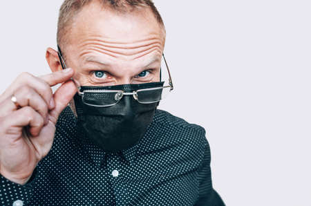 Portrait of man taking off glasses in black facial mask during a COVID-19 world pandemic looking at camera. Virus self-protection and vision health concept image.の写真素材