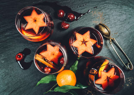Still-life top view with hot Mulled wine and spices, fruits, cinnamon served in thin glass mugs on the black textured stone table. Christmas and New Year celebration concept image.の写真素材
