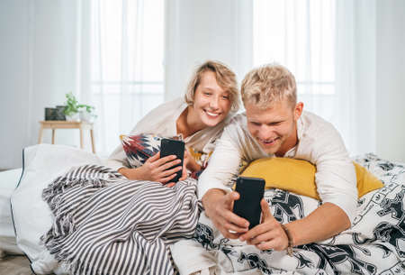 Teens couple lying in a cozy bed in the bedroom and browsing together internet or checking mails...