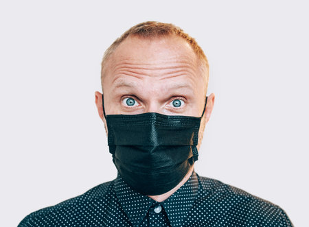 Portrait of surprised man in black facial mask during a COVID-19 world pandemic looking at camera. Self-protection and stop virus spreading measures concept imageの写真素材