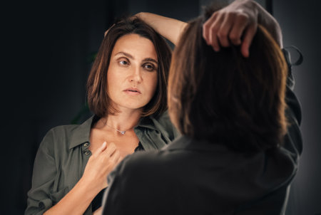 Sensual low key boudoir portrait of seductive female gazing on her mirror reflection as she ruffling hair. Human emotion or fashion concept image.の写真素材