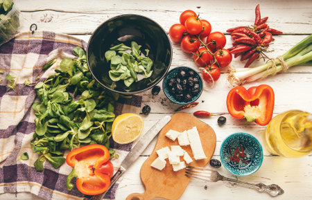 Vegetarian low-calorie Greek salad preparation white wooden table top view. Fresh soft cheese, cherry tomatoes, spinach, paprika, pickled olives chili pepper, paprika, olive oil are there.の写真素材