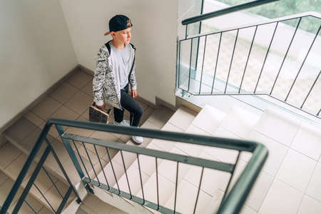Teenager skateboarder boy with a skateboard going up by staircase home. Youth generation Freetime spending concept image.の写真素材