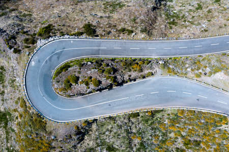 Top view aerial drone image of asphalt road 180 degrees curve surrounded by cliffs on Madeira...