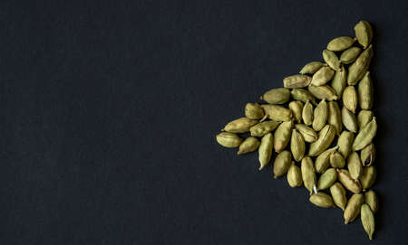 Close up photo of Cardamom pods pile formed as PLAY sign icon on the matt black background. Cardamom...