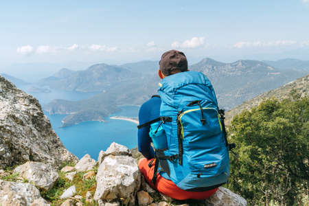 Backpacker man sitting on clifftop and enjoying the Mediterranean Sea Oludeniz town Bay during Lycian Way trekking walk. Famous Likya Yolu Turkish route near Letoon. Active people vacation concept.の写真素材