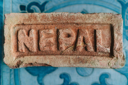 "NEPAL" inscription on the old Terra cotta color brick lying on blue tile flooring. Building industry and Asian country traveling close-up concept image.の写真素材