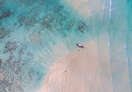 Aerial shot of the Mnemba Island white sand sandbanks washed with turquoise Indian ocean waves near the Zanzibar island, Tanzania. The couple came here on the motorboat, anchored it and having rest.の写真素材