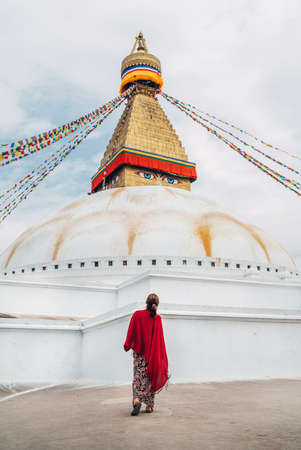Female dressed long summer dress with red shawl walking by square near Boudhanath Stupa - the largest spherical stupas in Nepal. Traveling around the world concept image.の写真素材
