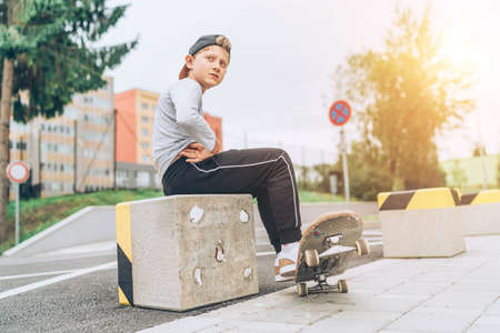 Teenager skateboarder boy portrait in a baseball cap with old skateboard on the city street. Youth generation Free time spending and an active people concept image.の写真素材