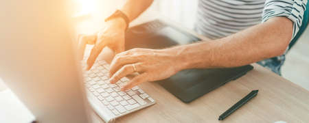 Writer typing modern computer keyboard writing novel sitting at the white wood table. Distance or freelance work on worldwide quarantine time conceptの写真素材