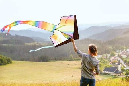 Teenager boy on the meadow grass and preparing colorful rainbow kite toy for flying. Happy childhood moments or outdoor time spending concept image.の写真素材