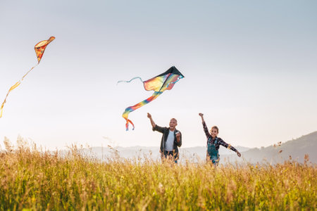 Outdoor portraits of a girl with father while they running with colorful kites by the high grass meadow sincerely laughing. Warm family moments or outdoor time spending concept image.の写真素材