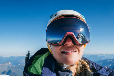 High altitude mountaineer smiling female portrait in safe ski helmet and goggles on the Mont Blanc 4810m with picturesque Alpine mountains background. Active sporty people and success concept imageの写真素材