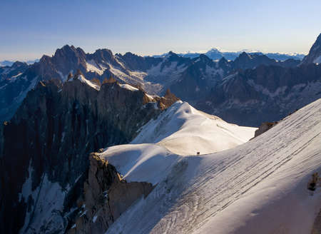 French Alps mountains peaks panorama view with silhouettes of climbers as roping team descending on the snowy slope under Aiguille du Midi 3842m. Beauty of Nature and extreme people activity concept.の写真素材