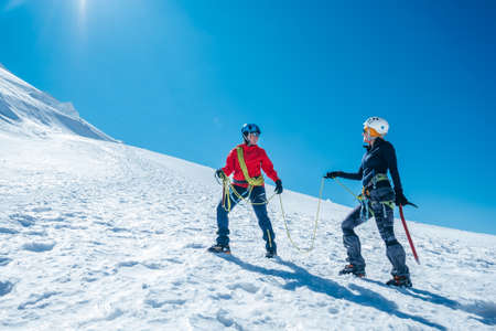 Two laughing to each other young women Rope team ascending Mont blanc du Tacul summit 4248m dressed mountaineering clothes with ice axes on snowy slopes. People extreme activities sporty concept imageの写真素材