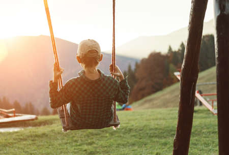 Little Boy swinging on the mountain kids park playground in the evening sunset rays. Careless childhood concept imageの写真素材