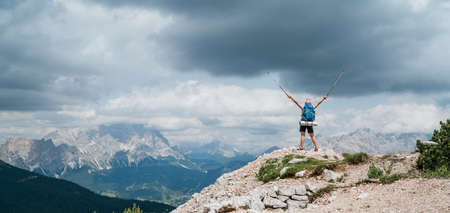 Woman trekker with backpack rose arms up with trekking poles enjoying picturesque Dolomite Alps view near Tre Cime di Lavaredo formation in South Tyrol, Italy. Active people and mountain concept.の写真素材