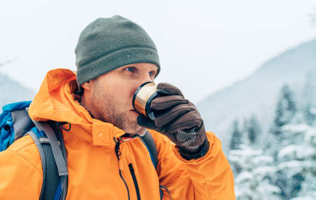 Man drinking a hot drink from flask dressed bright orange softshell jacket while he trekking winter mountains route. Active people in the nature concept image.の写真素材