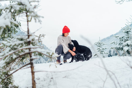 A young woman in warm knitted clothes walking her 2 dogs in a picturesque snowy mountain outdoor. Female smiling and playing with pets. Human and pets winter concept imageの写真素材