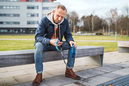 Broken with grief man as a dog owner is grieving sitting on a bench with the lovely pet collar and leash, deep weeping about animal loss. Lovely home pets and sorrow concept.の写真素材