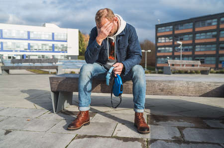 Broken with grief man dog owner is grieving sitting on a bench with the lovely pet collar and deep weeping about animal loss. Home pets relatives and love concept.の写真素材
