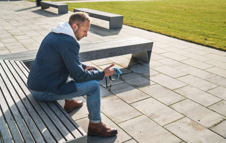 Broken with grief man as a dog owner is grieving sitting on a bench with the lovely pet collar and leash, deep weeping about animal loss. Lovely home pets and sorrow concept.の写真素材