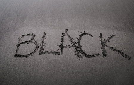 BLACK word handwritten inscription on the black sand Madeira beach as a Black Friday sales concept.