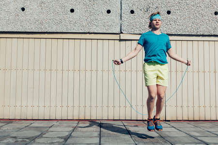 Young teenager boy jumping by the skipping rope on the house roof. Modern people fit challenges concept image.の写真素材