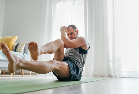 Young muscular body man doing "bicycle" abs muscles exercise on the living room floor. Healthy lifestyle or sporty people concept image.の写真素材
