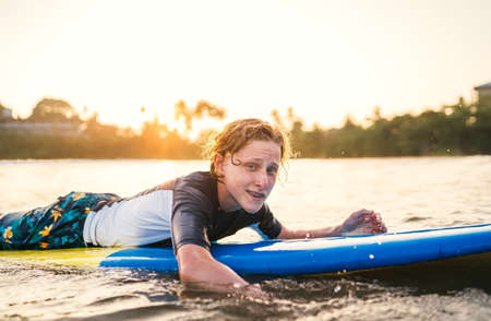 Portrait of a teen boy with Dental braces floating on surfboard. He is smiling. Happy childhood and active vacation time concept.の写真素材