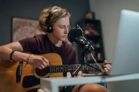 Home sound studio young teenager portrait playing guitar in Headphones with the microphone on the foreground. Modern audio recording technology concept image.の写真素材