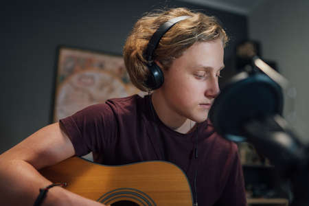 Home sound studio young teenager portrait playing guitar in Headphones and recording music using...