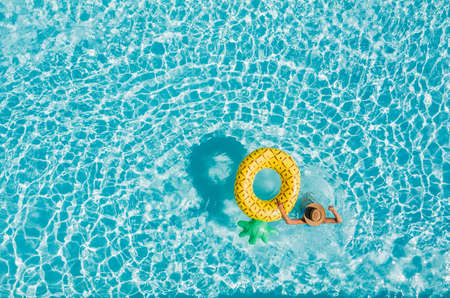 Top view of a young female in swimsuit bikini in a straw hat on blue swimming pool waves background with big inflatable Yellow Pineapple tube. Chill out a summer vacation in luxury resorts concept.の写真素材