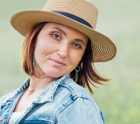 The portrait of a middle-aged smiling woman looking at the camera. She dressed in a jeans jacket, straw hat. Natural people beauty concept image.の写真素材